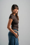 Woman wearing a brown shirt and blue jeans against a gray background