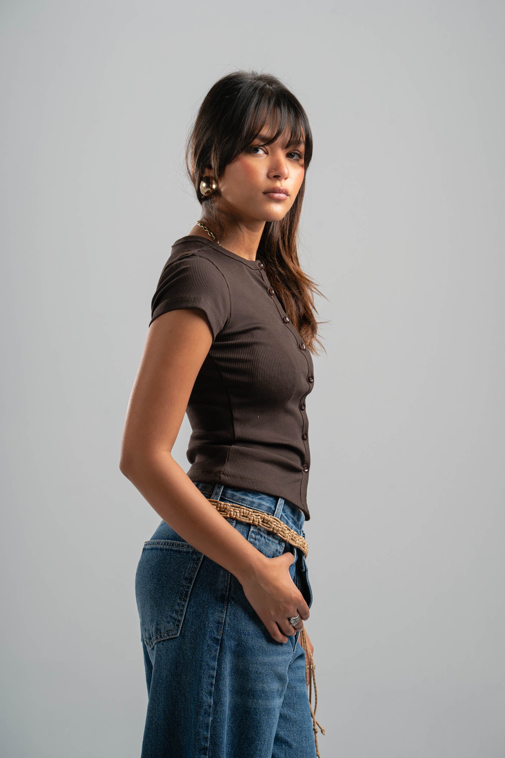 Woman wearing a brown shirt and blue jeans against a gray background