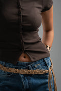 Person wearing a brown shirt and blue jeans with a braided belt on a gray background