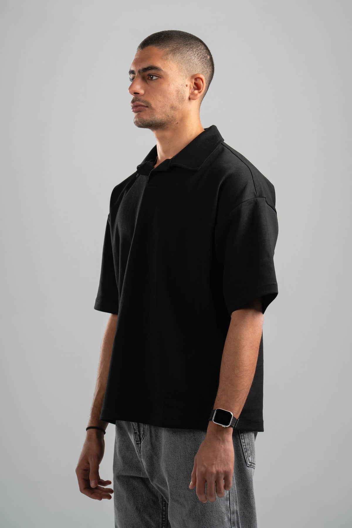Man wearing a black polo shirt and gray pants against a gray background