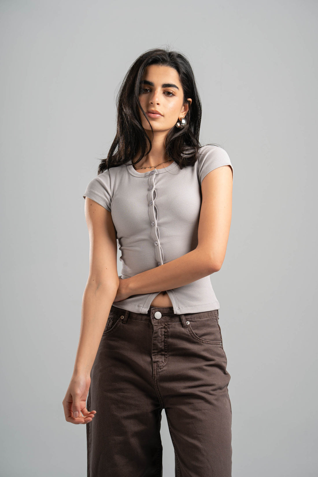 Woman wearing a gray t-shirt and brown pants against a gray background