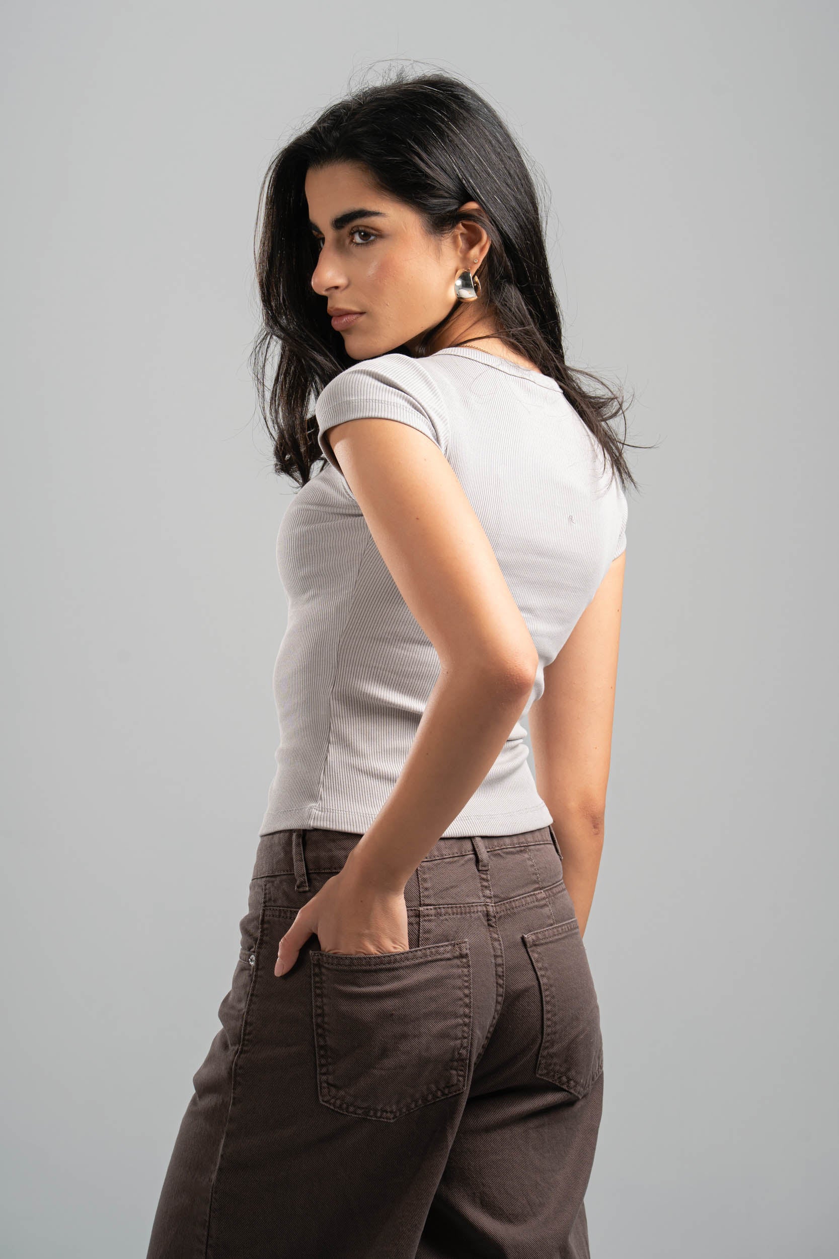 Woman wearing a white t-shirt and brown pants against a gray background