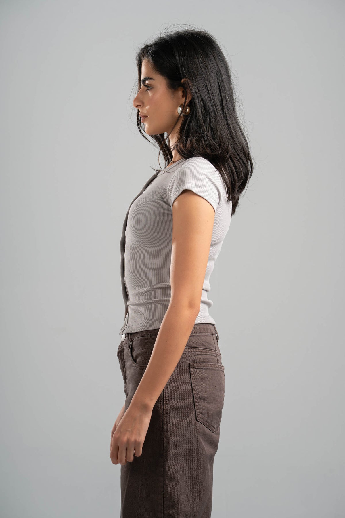 Woman wearing a gray t-shirt and brown pants against a gray background