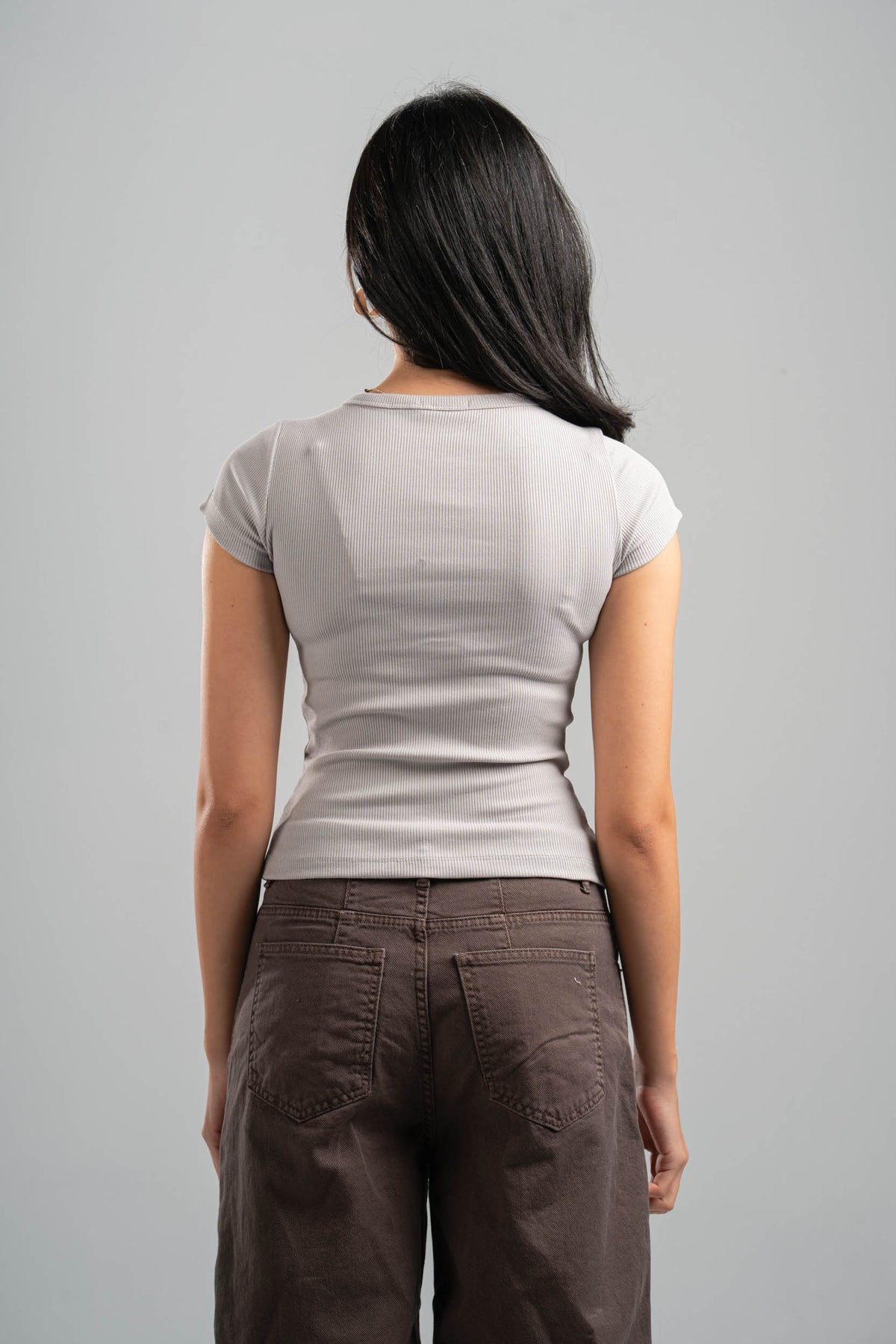 Person wearing a light gray t-shirt and brown pants against a gray background