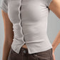 Person wearing a light gray ribbed shirt with buttons and brown pants on a gray background