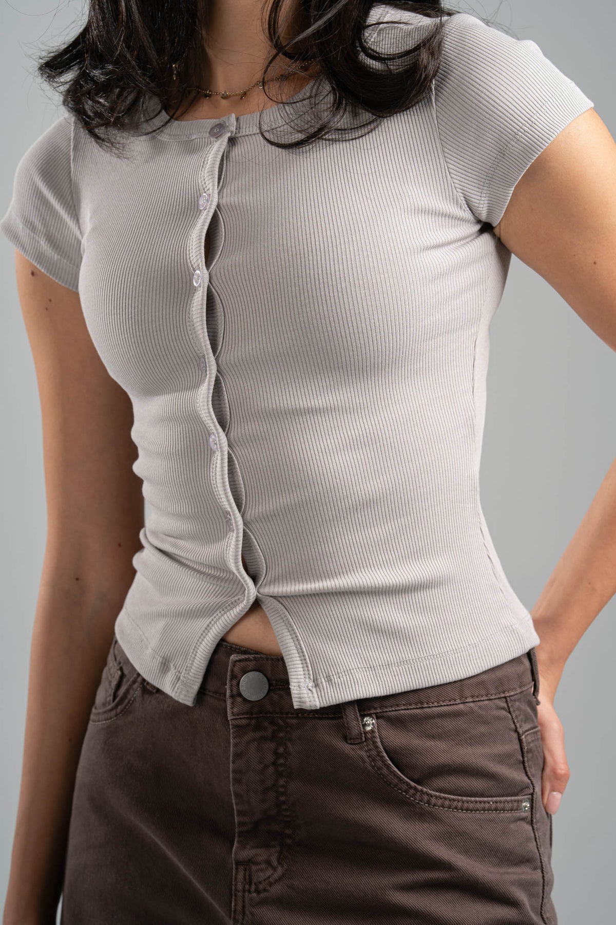 Person wearing a light gray ribbed shirt with buttons and brown pants on a gray background