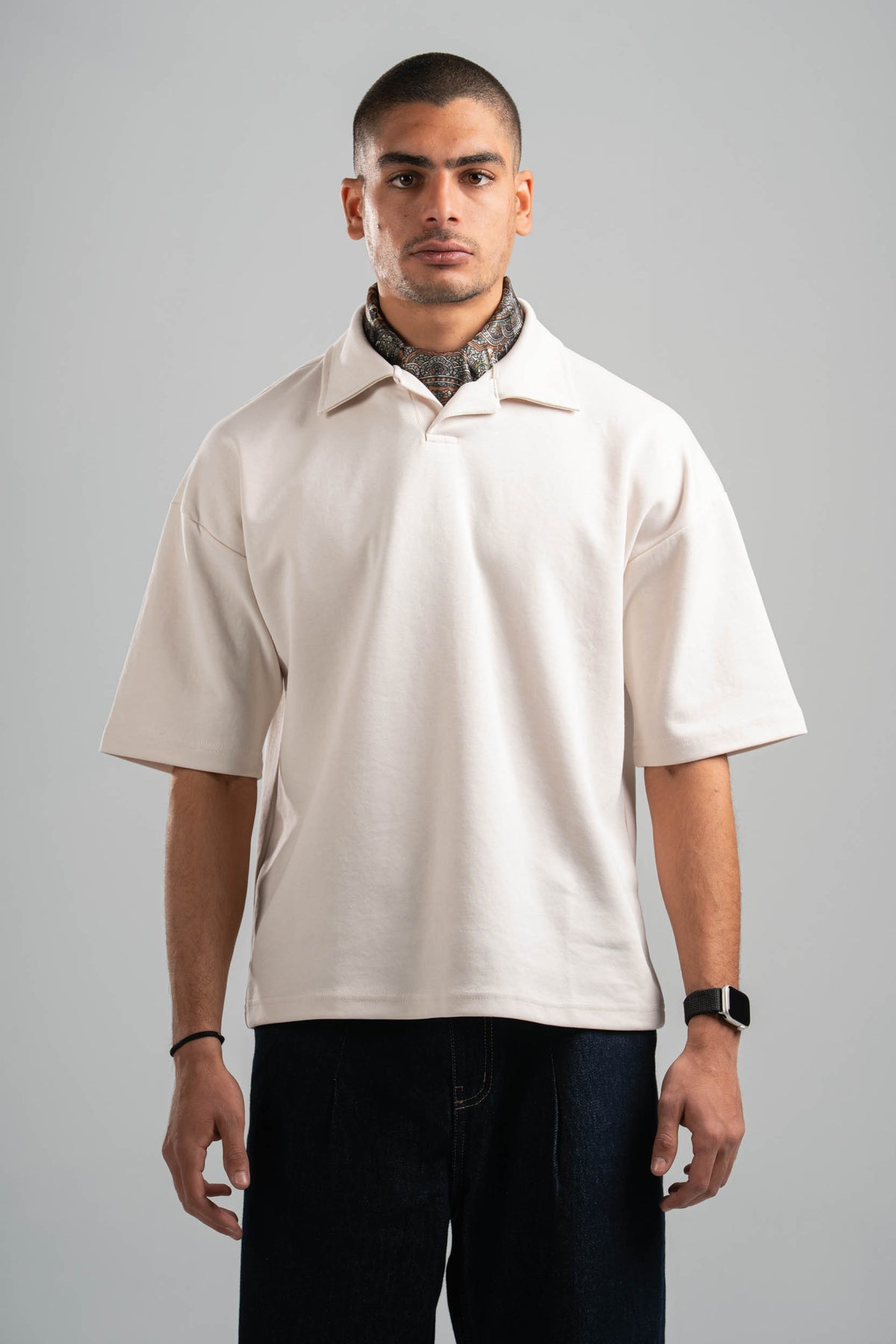 Man wearing a beige short-sleeve shirt and dark pants on a gray background