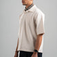 Man wearing a beige polo shirt and dark pants against a gray background