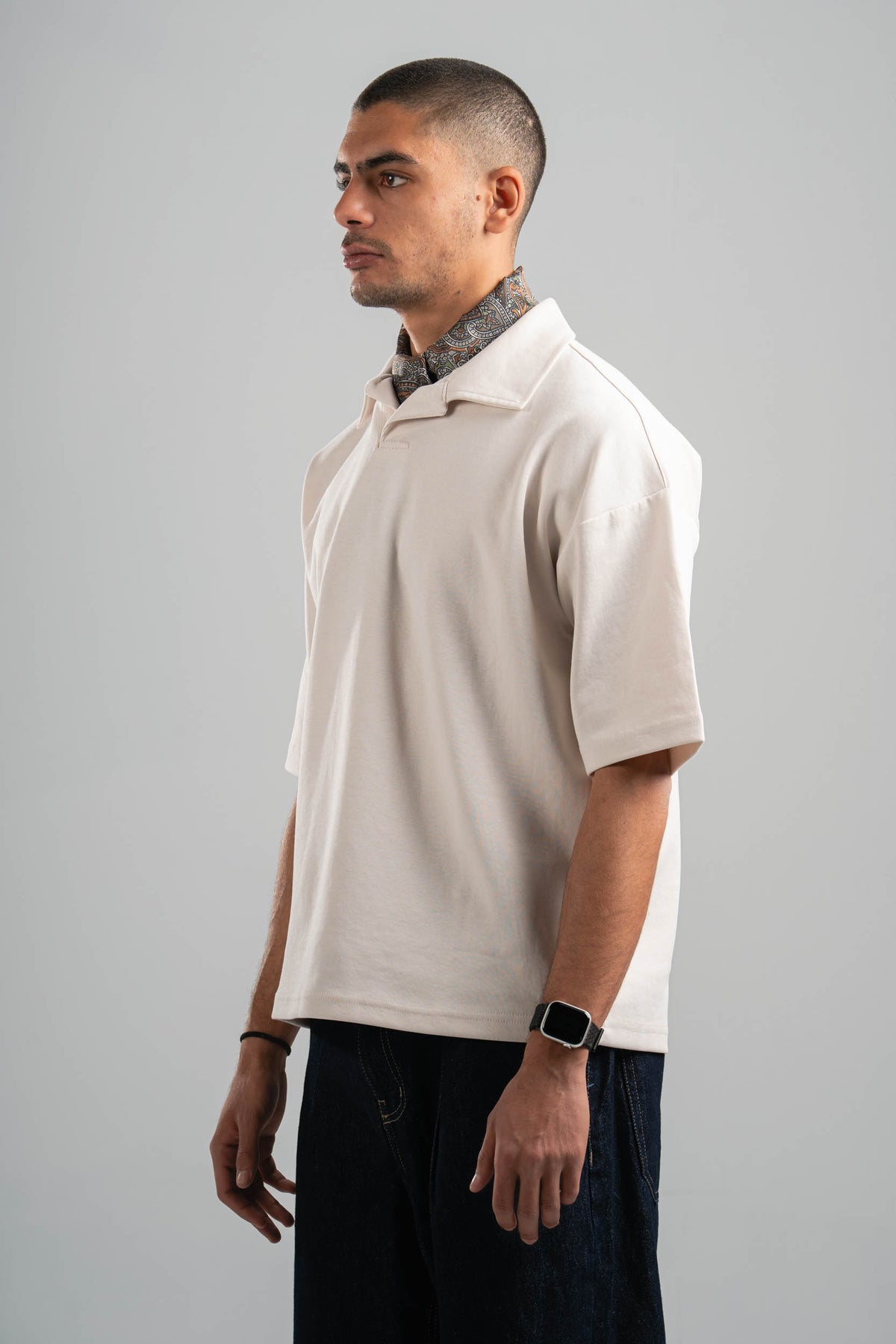 Man wearing a beige polo shirt and dark pants against a gray background
