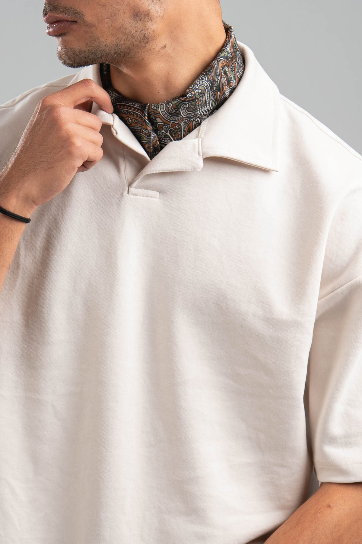 Person wearing a white shirt with a patterned scarf around their neck against a gray background