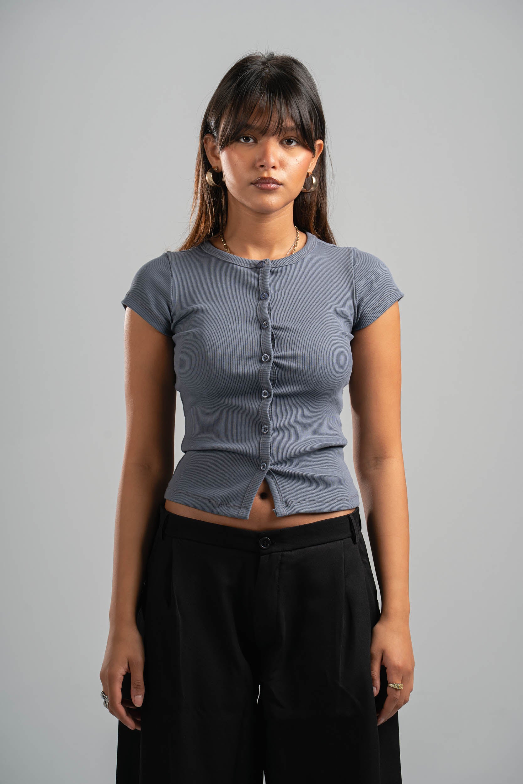 Woman wearing a gray short-sleeve top and black pants against a gray background