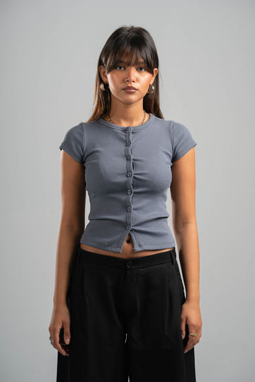 Woman wearing a gray short-sleeve top and black pants against a gray background