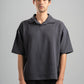 Man wearing a dark gray oversized polo shirt against a plain background