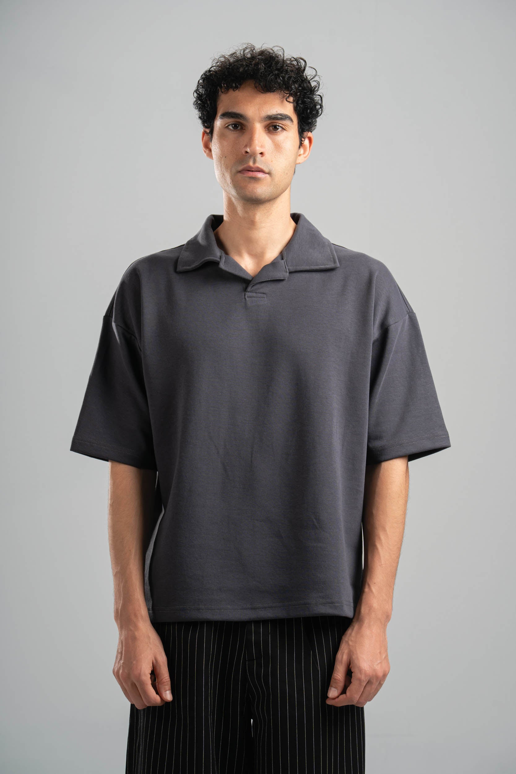 Man wearing a dark gray oversized polo shirt against a plain background