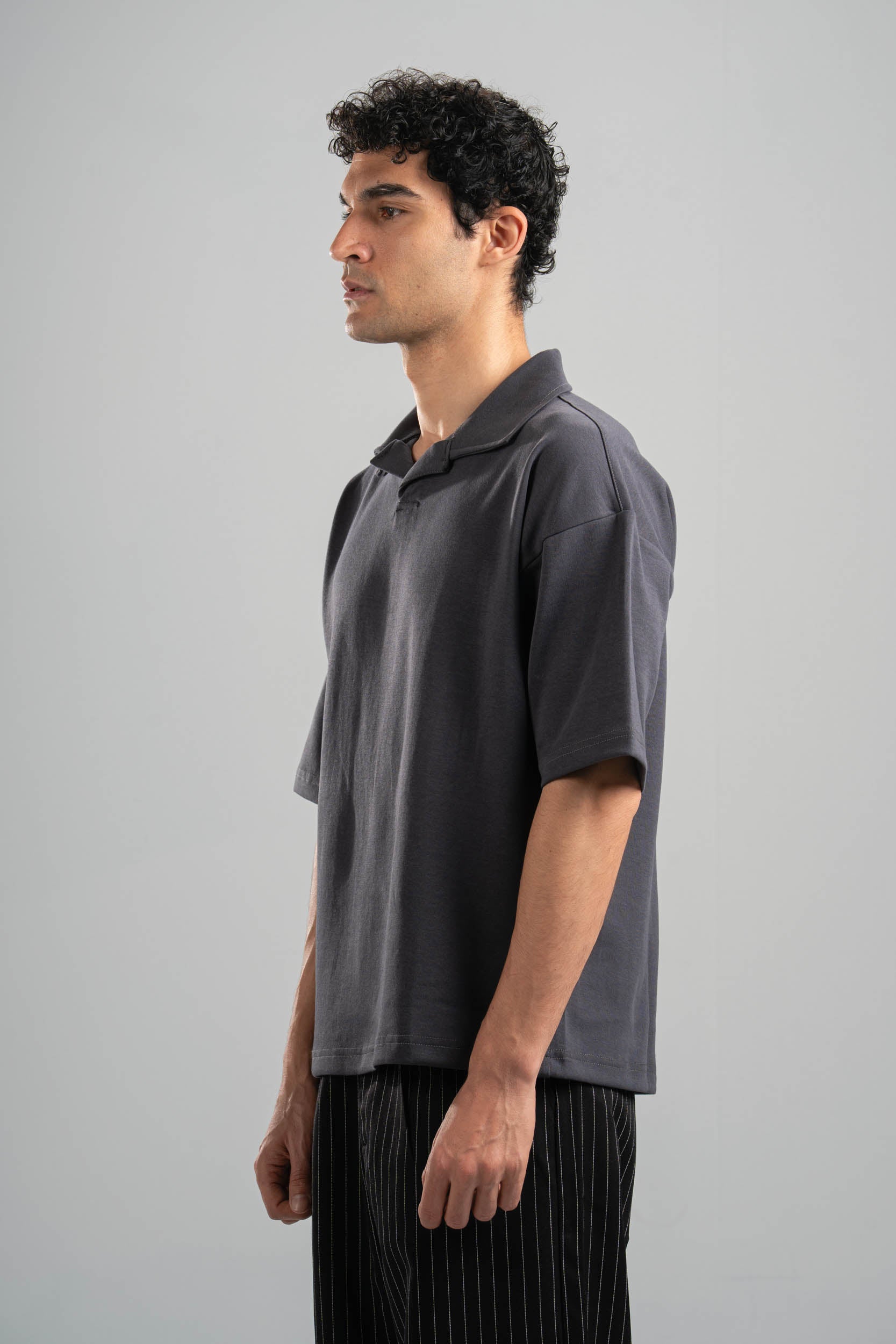 Man wearing a dark gray polo shirt and black pants against a plain background