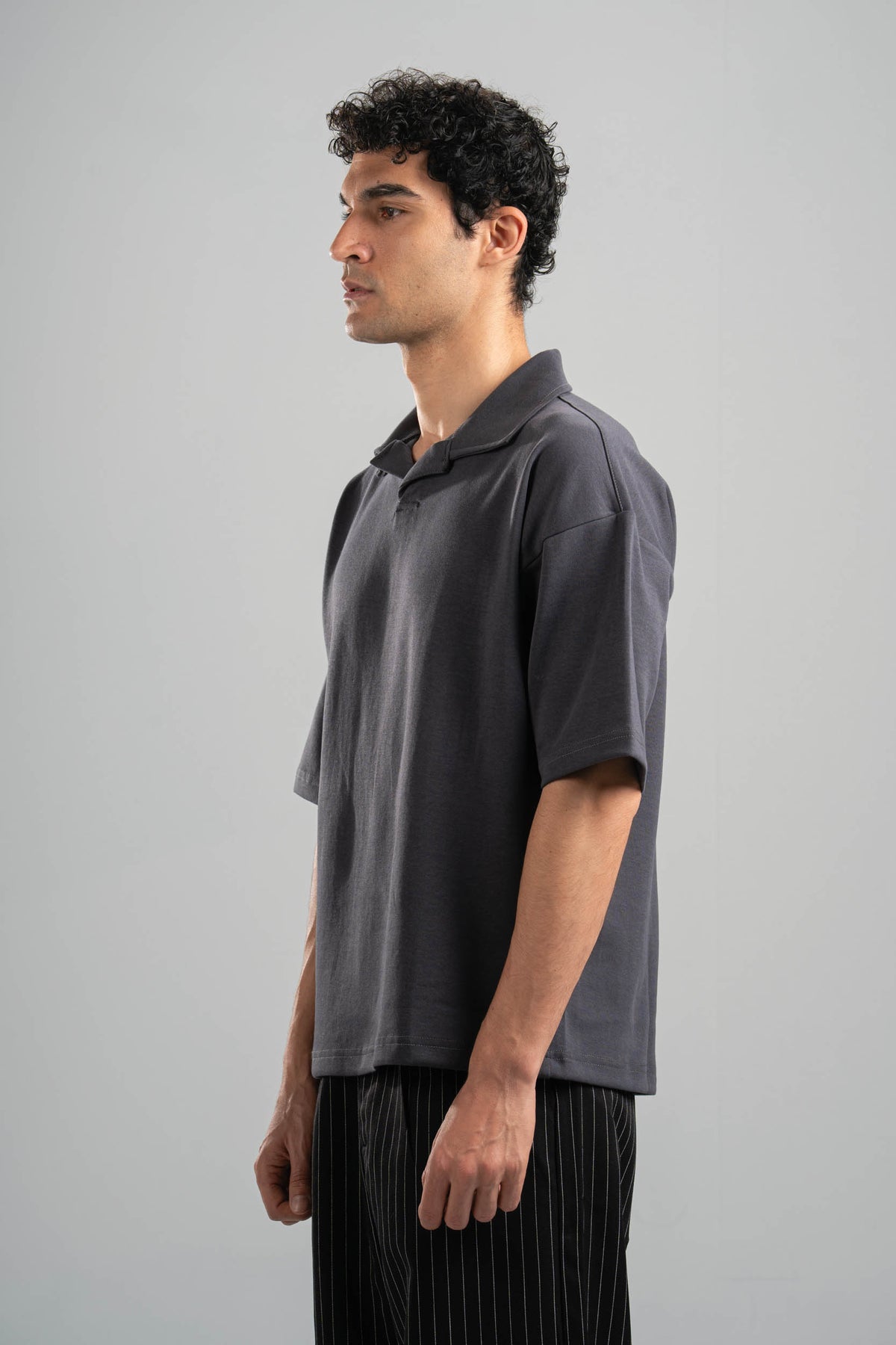 Man wearing a dark gray polo shirt and black pants against a plain background