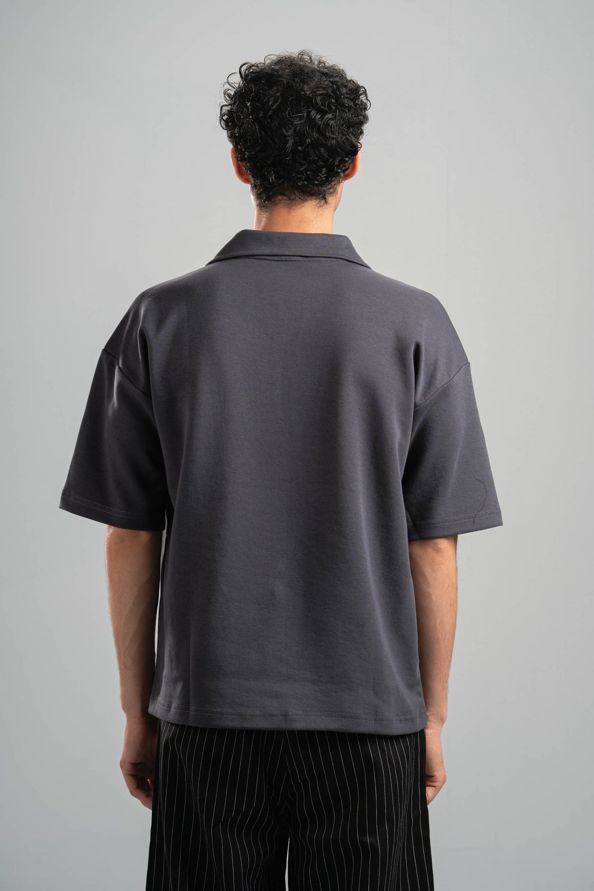 Person wearing a gray polo shirt from behind on a plain background
