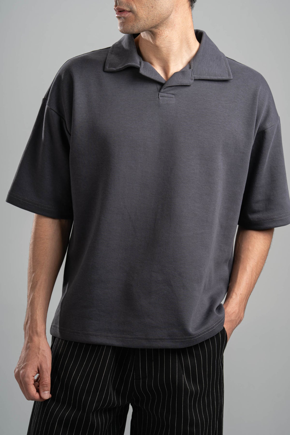 Person wearing a dark gray polo shirt against a gray background