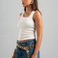 Woman wearing a white tank top and blue jeans with a decorative belt on a gray background