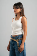 Woman wearing a white tank top and blue jeans with a decorative belt on a gray background