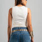 Woman wearing a white sleeveless top and blue jeans with a belt on a gray background