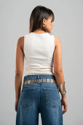 Woman wearing a white sleeveless top and blue jeans with a belt on a gray background