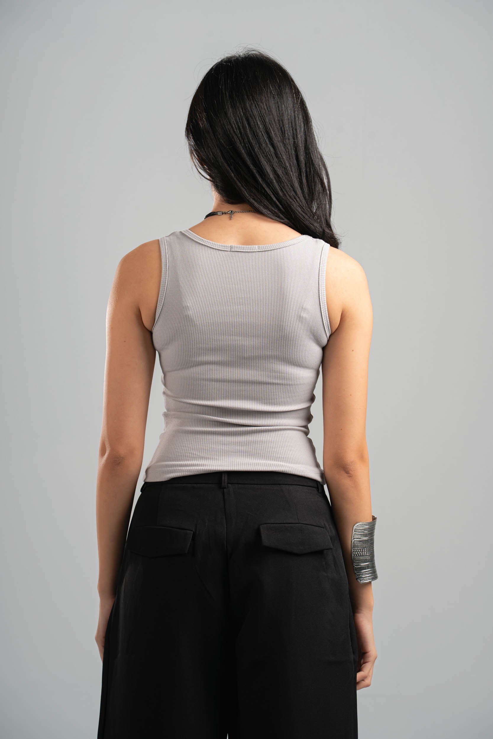 Person wearing a gray sleeveless top and black pants on a gray background