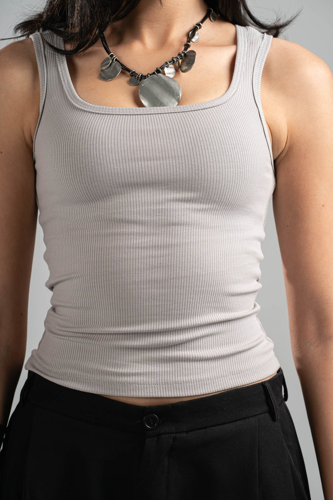 Woman wearing a gray tank top and black pants on a gray background