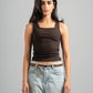 Woman wearing a brown tank top and light blue jeans against a gray background