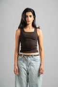 Woman wearing a brown tank top and light blue jeans against a gray background