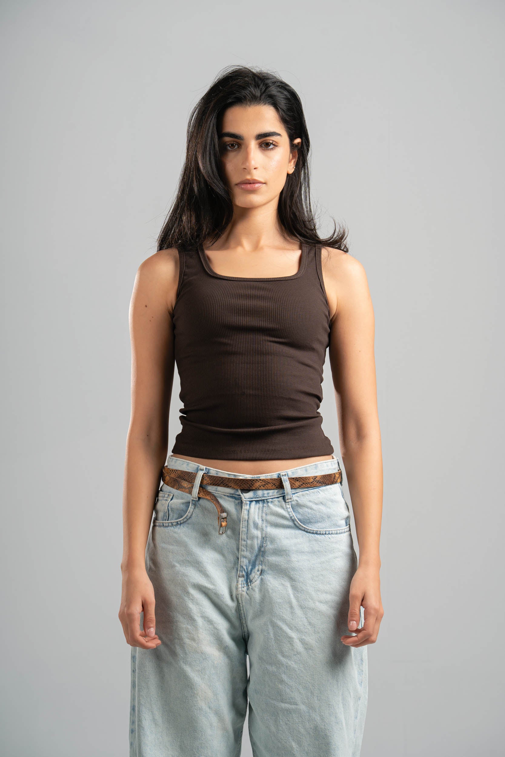Woman wearing a brown tank top and light blue jeans against a gray background