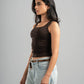 Woman wearing a brown tank top and light blue jeans against a gray background