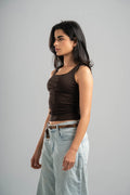 Woman wearing a brown tank top and light blue jeans against a gray background