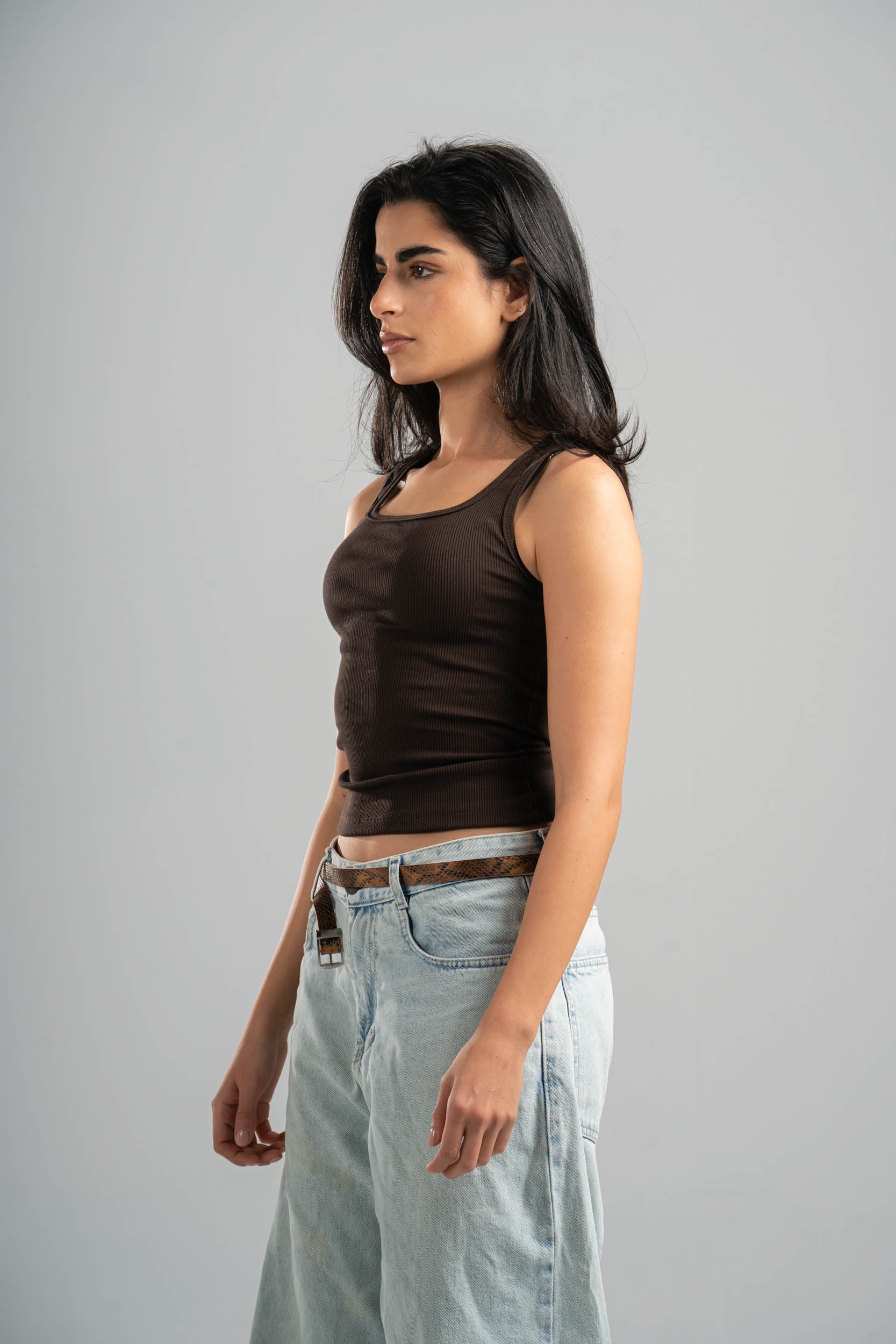 Woman wearing a brown tank top and light blue jeans against a gray background