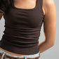 Person wearing a brown tank top and light blue jeans against a gray background