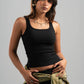 Woman wearing a black tank top and holding a green jacket against a gray background