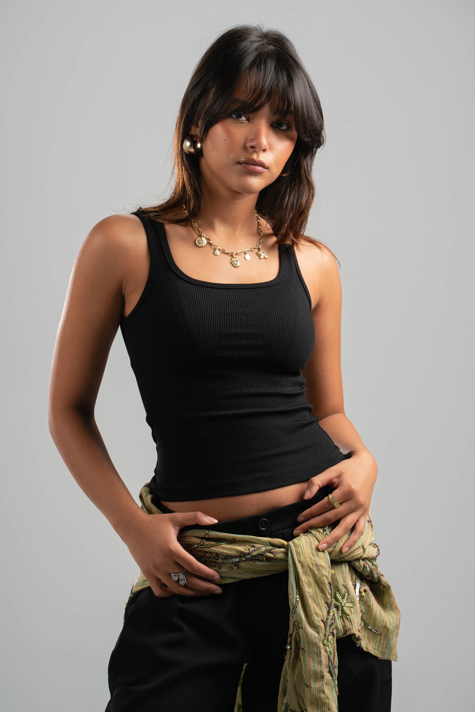 Woman wearing a black tank top and holding a green jacket against a gray background