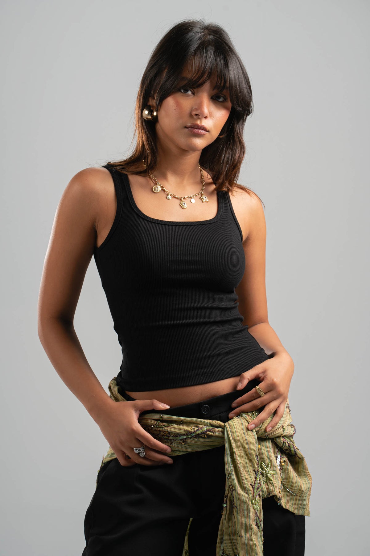 Woman wearing a black tank top and holding a green jacket against a gray background