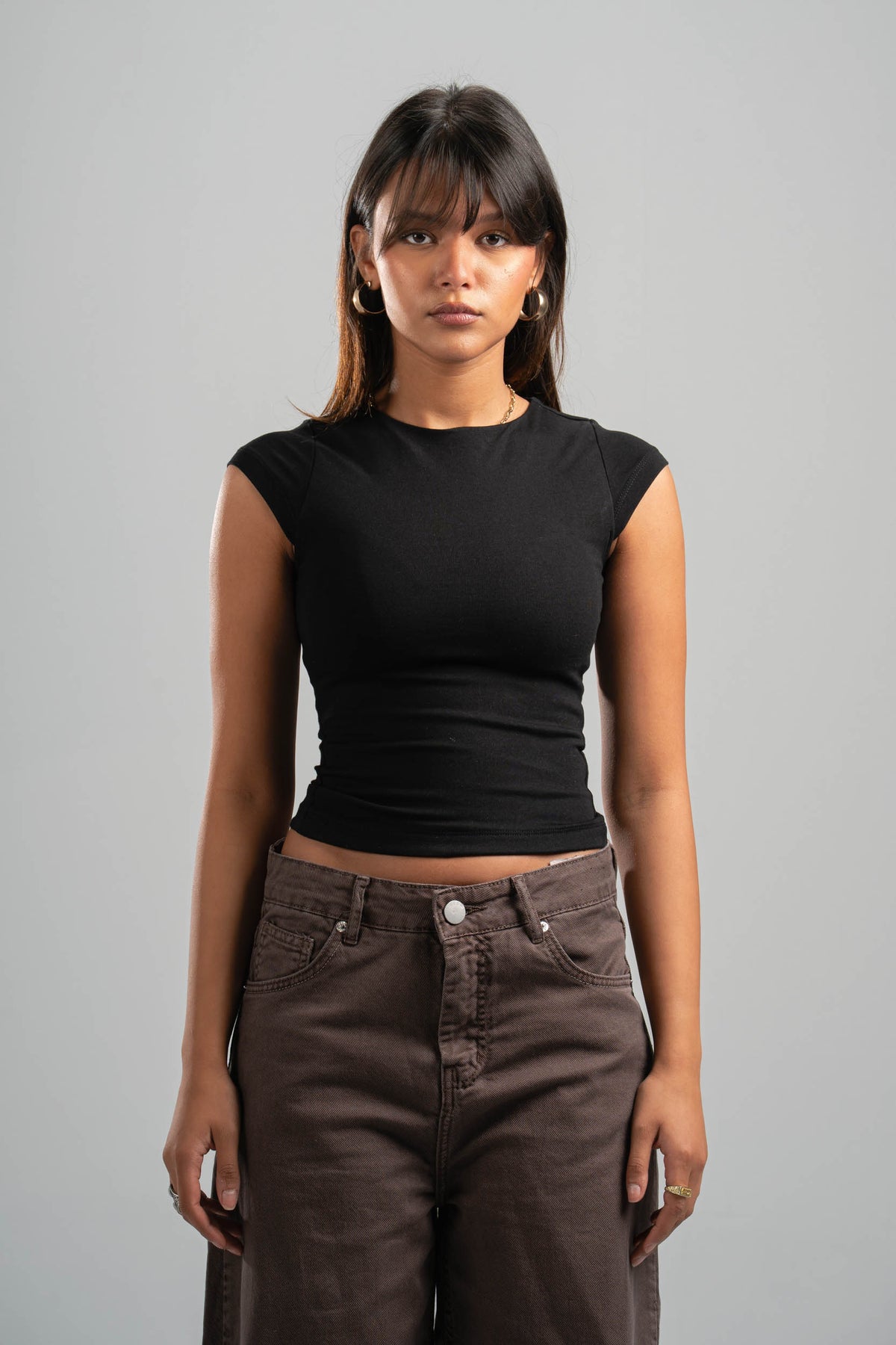 Woman wearing a black top and brown pants against a gray background