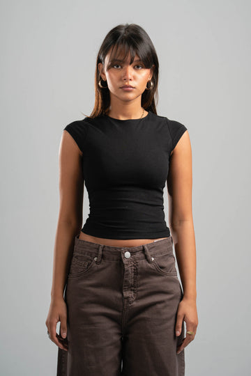 Woman wearing a black top and brown pants against a gray background