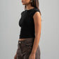 Woman wearing a black sleeveless top and brown pants against a gray background