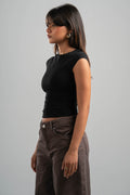 Woman wearing a black sleeveless top and brown pants against a gray background
