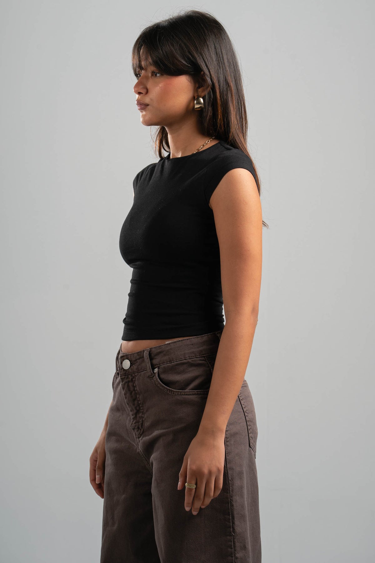 Woman wearing a black sleeveless top and brown pants against a gray background