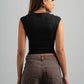 Woman wearing a black sleeveless top and brown pants against a gray background