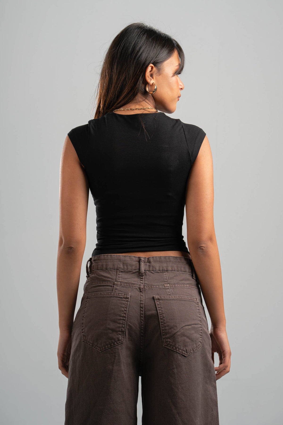 Woman wearing a black sleeveless top and brown pants against a gray background