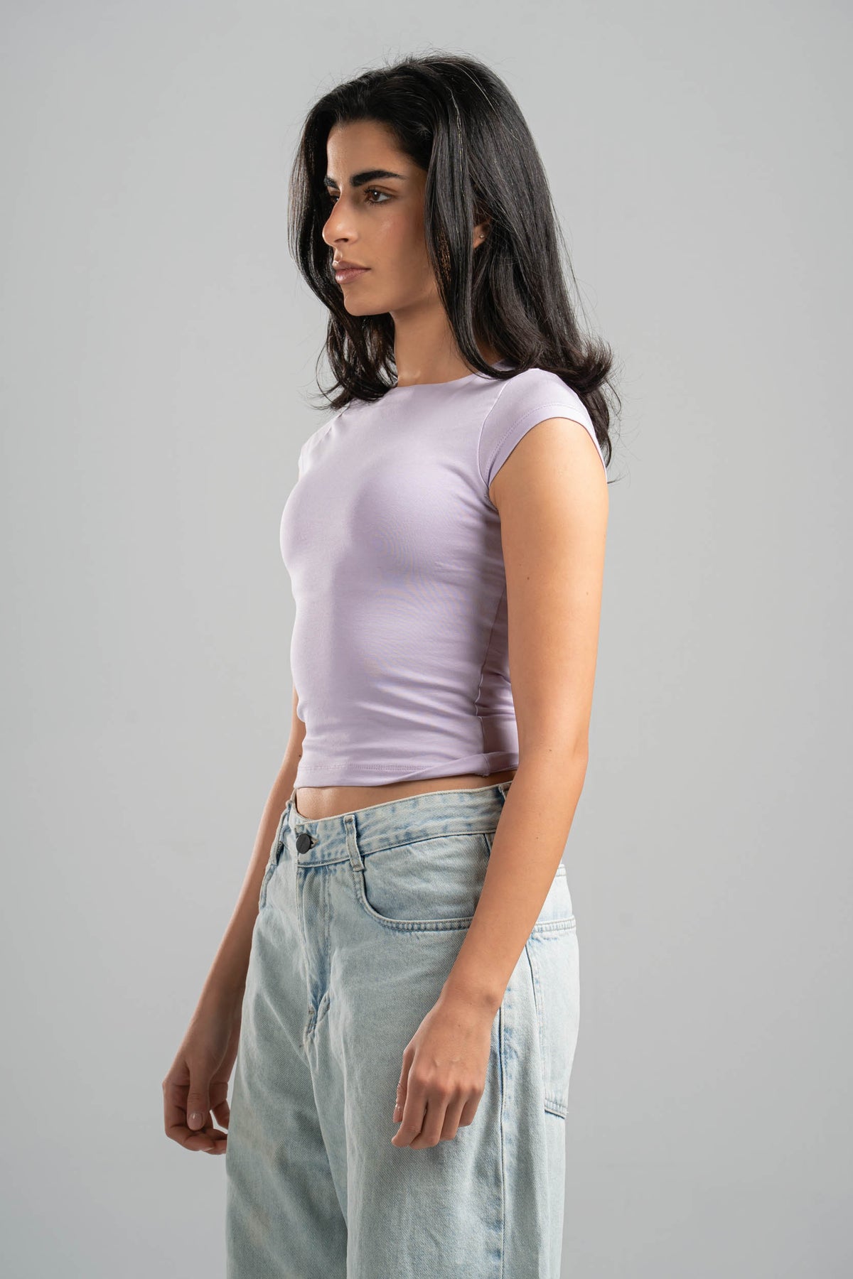 Woman wearing a light purple crop top and light blue jeans against a gray background