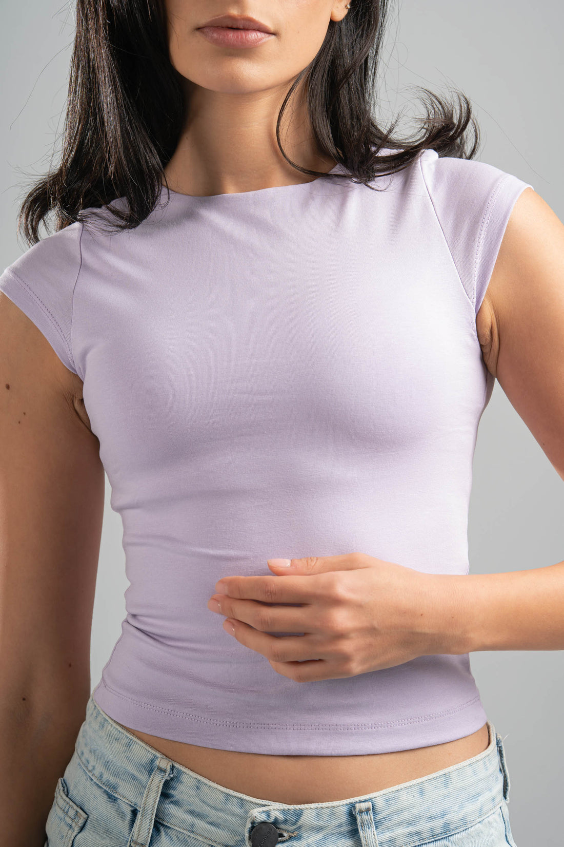 Woman wearing a light purple sleeveless top and light blue jeans against a gray background