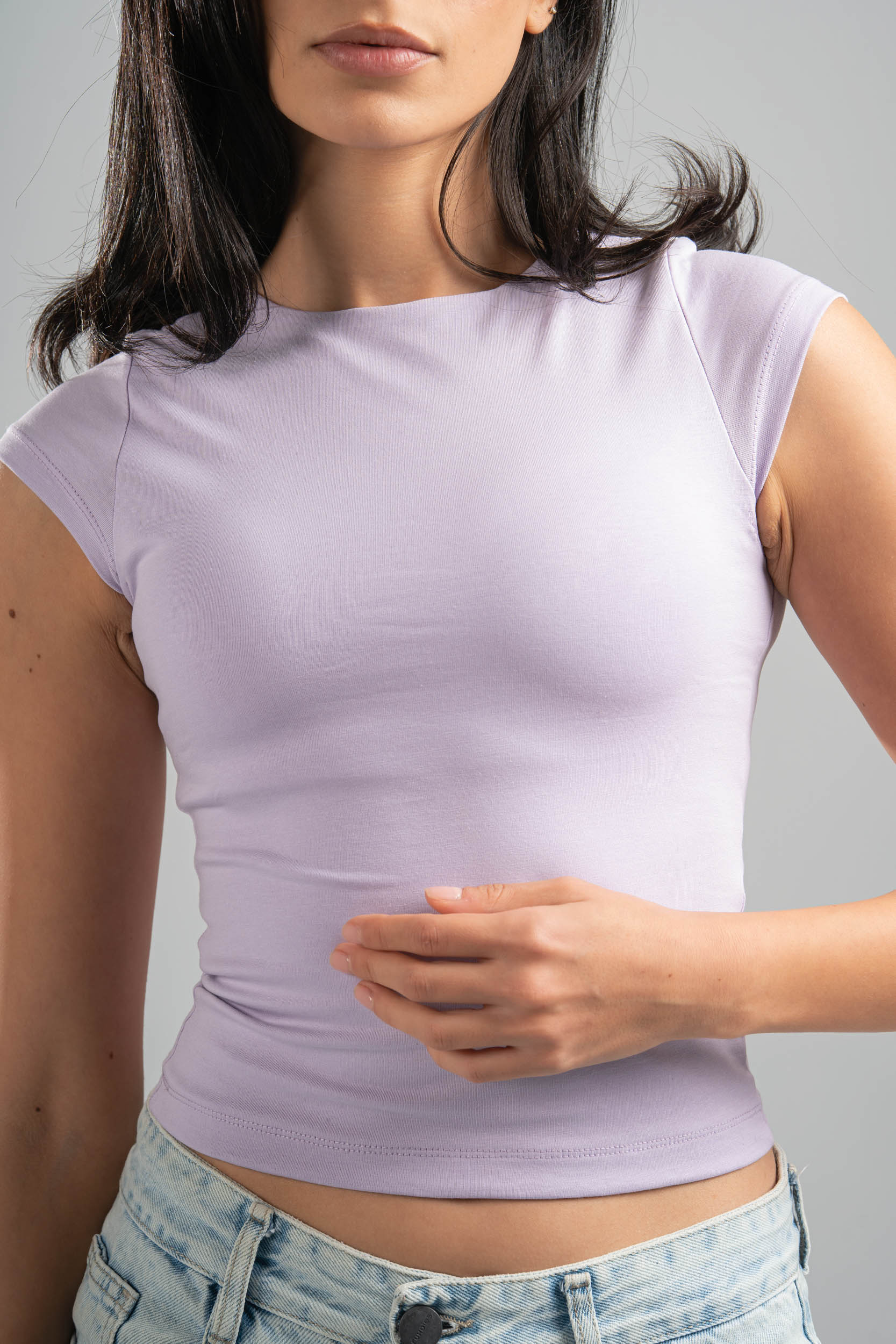 Woman wearing a light purple crop top and denim shorts against a gray background
