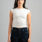 Woman wearing a white sleeveless top and dark jeans against a gray background