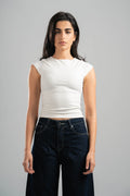 Woman wearing a white sleeveless top and dark jeans against a gray background